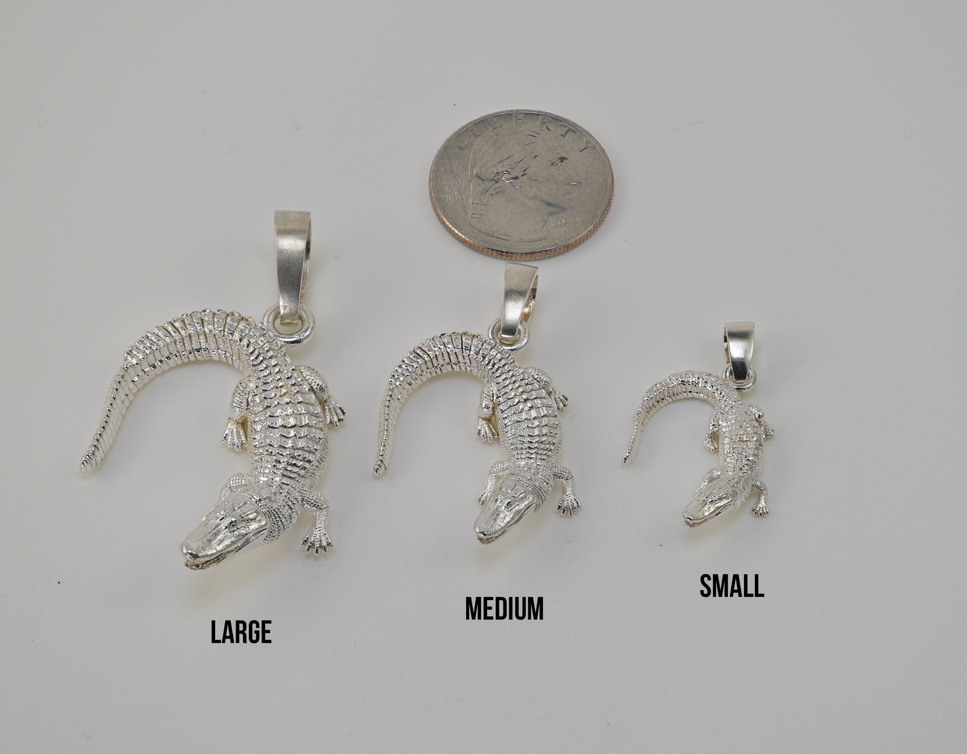 Three silver alligator pendants in large, medium, and small sizes are displayed on a light gray background with a quarter coin above them for scale and size labels 'LARGE', 'MEDIUM', and 'SMALL' underneath.