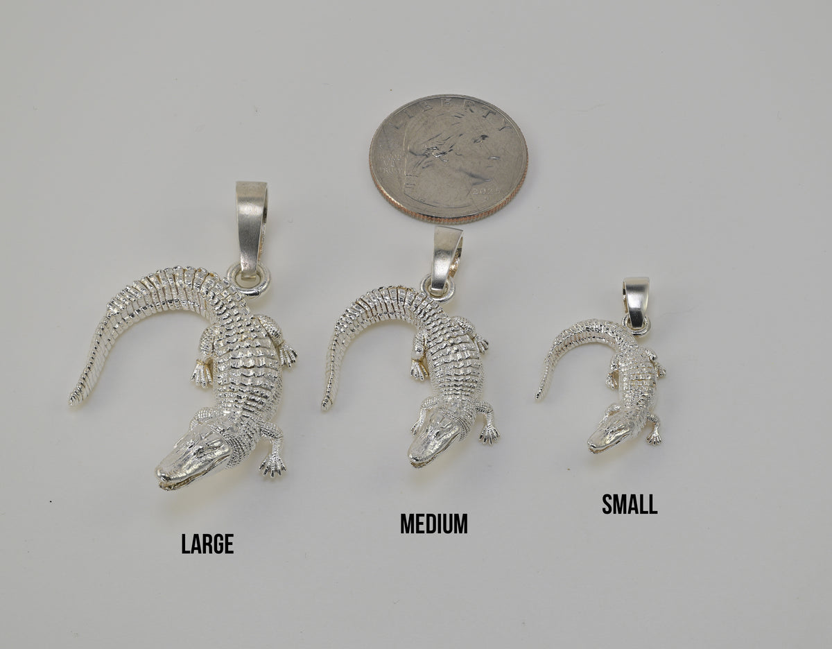 Three silver alligator pendants in large, medium, and small sizes are displayed on a light gray background with a quarter coin above them for scale and size labels 'LARGE', 'MEDIUM', and 'SMALL' underneath.