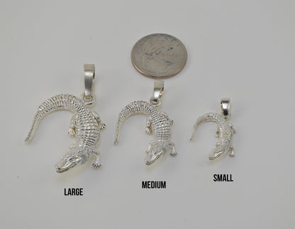 Three silver alligator pendants in large, medium, and small sizes are displayed on a light gray background with a quarter coin above them for scale and size labels 'LARGE', 'MEDIUM', and 'SMALL' underneath.
